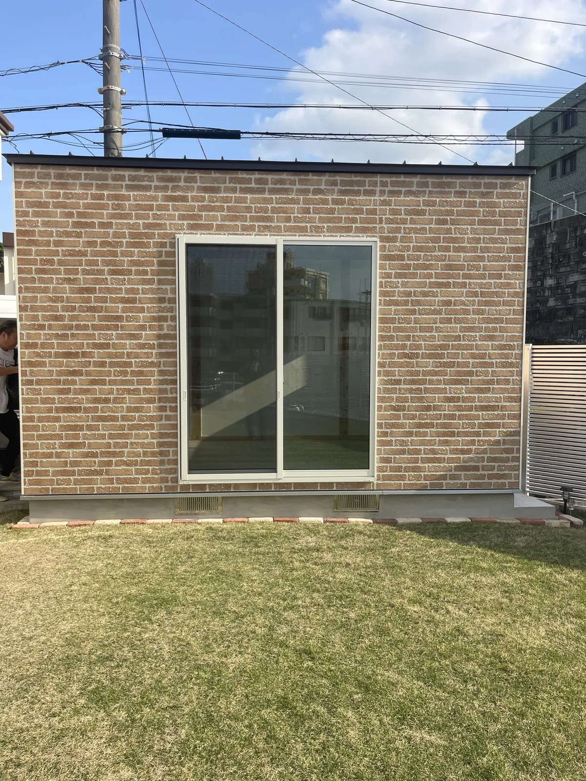 芝生の庭に建つ、レンガ調の外壁と大きな引き違い窓の小屋
