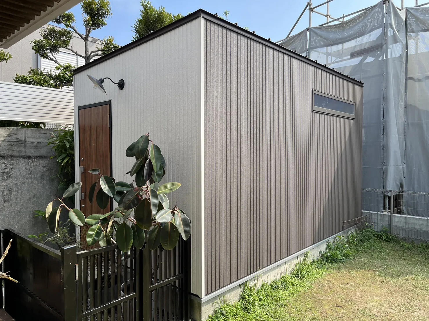 芝生の庭に建つ、グレージュの外壁と木の扉の小屋