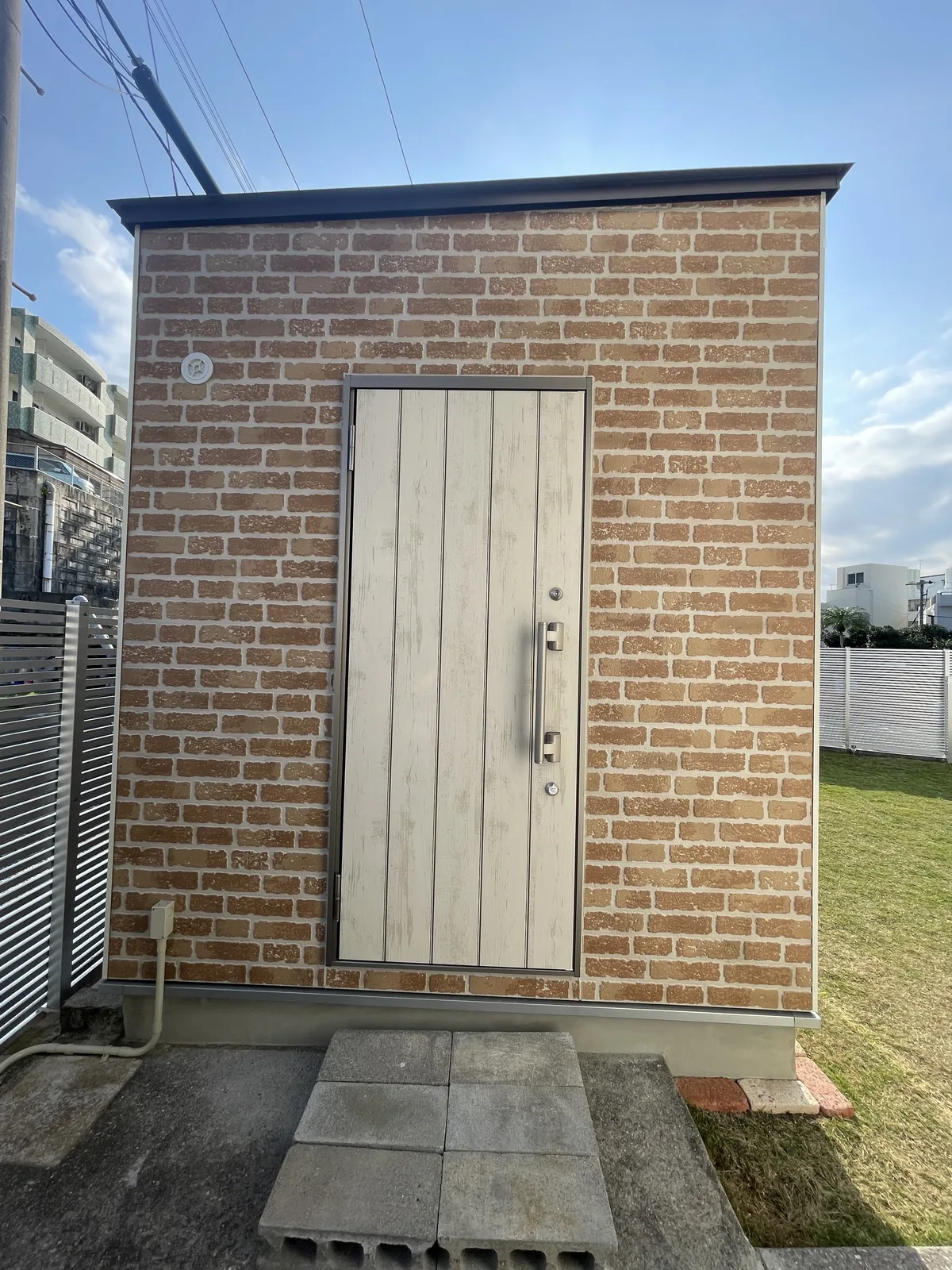 街なかの敷地に建つ、レンガ調の外壁と白い扉の小屋